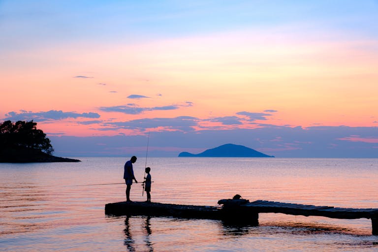 Father and Son Fishing on Sea Shore at Sunset