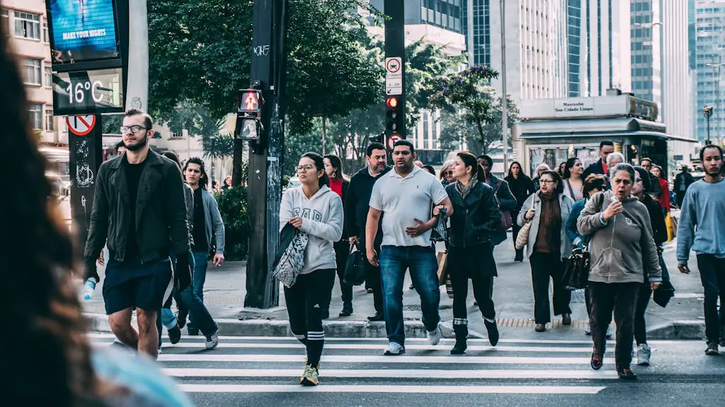 A diverse group of people crossing a street in a bustling city setting with skyscrapers.