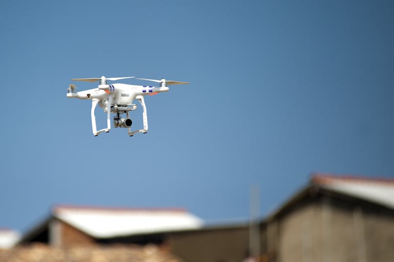 Aerial drone with camera hovering over rooftops beneath a clear blue sky, showcasing modern technology in action.