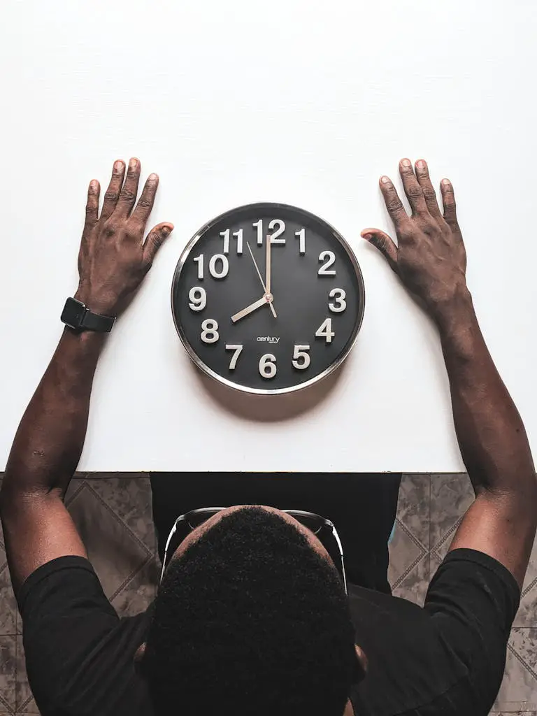 High angle view of a man with an apple watch observing a clock on a white table.