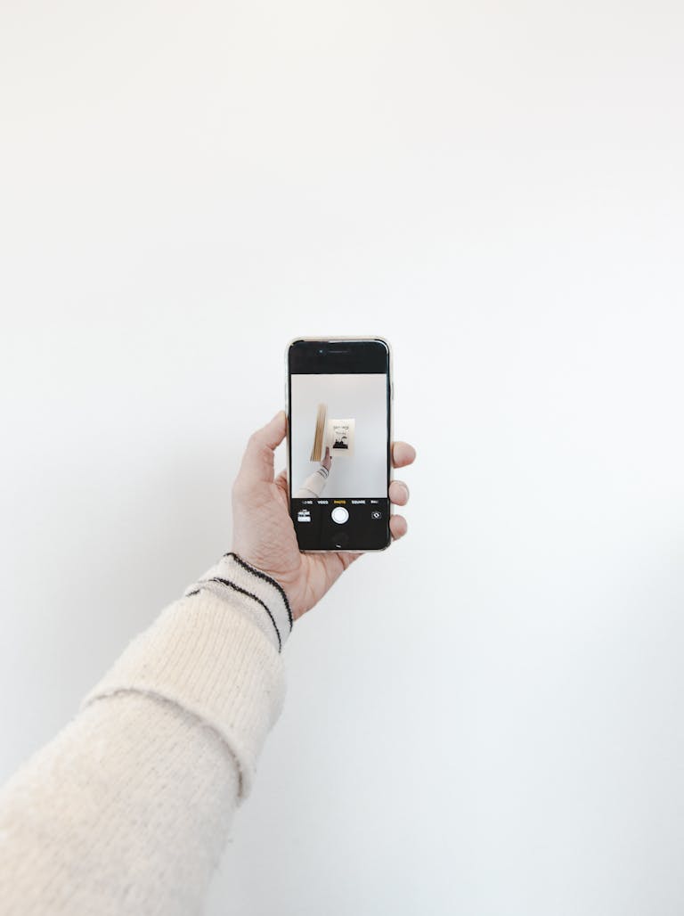 Minimalist photo featuring a hand holding a smartphone capturing an artistic shot indoors.