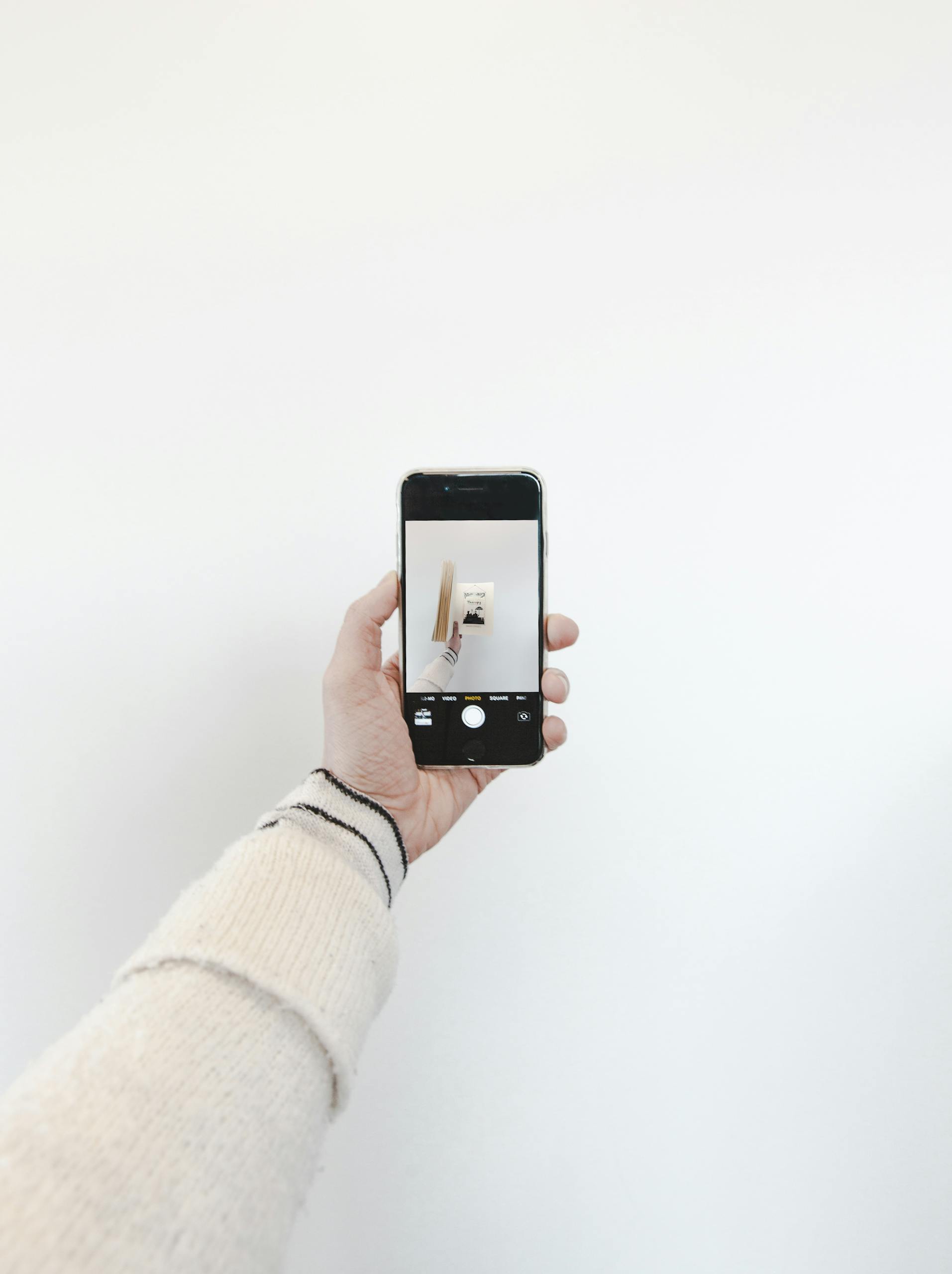 Minimalist photo featuring a hand holding a smartphone capturing an artistic shot indoors.